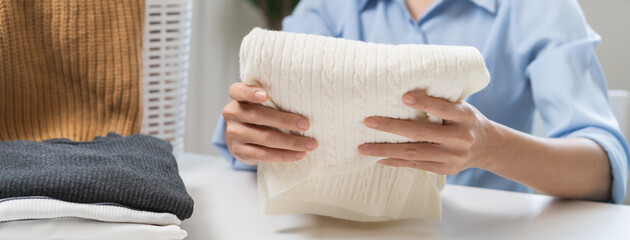 Housewife, asian young woman hand in many folding freshly shirts, sweaters or dress on desk, table after washing clean clothes and drying, making household working in room at home. Laundry and maid.