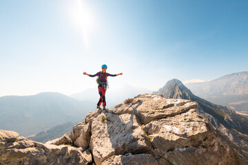 young girl climber in a helmet and with a backpack stands on top of a mountain. mountain climbing