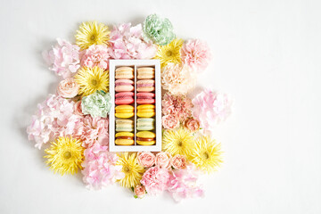 Dessert French Macarons in present box. Sweet dessert on a flowers background. Still life with macaroni cakes and different flower. Delivery concept, coffee and flower shop