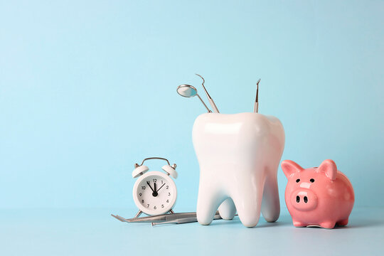 Tooth model with medical instruments, piggy bank and alarm clock on blue background. Investing in dental health care.
