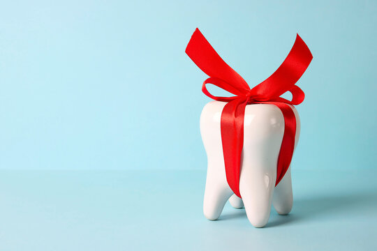 White tooth model with red bow ribbon on a blue background with copy space.