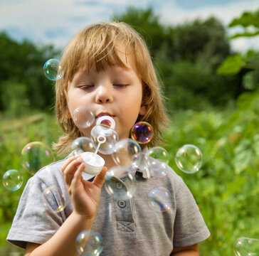 Happy Boy play in bubbles in field sunny summer day.
