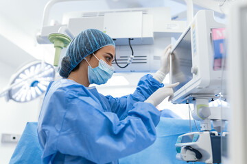 Portrait of a young female doctor in scrubs and a protective face mask preparing an anesthesia...