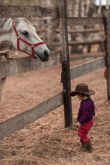 a horse in a stall with a child in a cowboy costume 