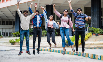 Cheerful group of graduated students jumping at college campus after completion of degree class or...