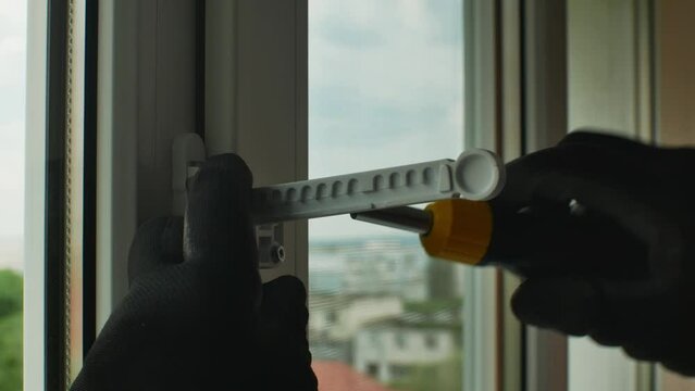 Male using screwdriver tightens screw that fixes plastic window opening limiter Close-up of gloved hand with screwdriver tightening window stopper fixing screw onto plastic window frame. Home repairs