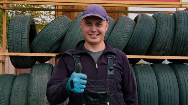 Portrait of a smiling man Auto mechanic showing Thumb signal with a cylinder wrench in his hand on the background of car tires detailing auto repair