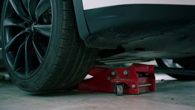 White luxury car being lifted with a red wheel change jack at a car service during detailing and dry cleaning