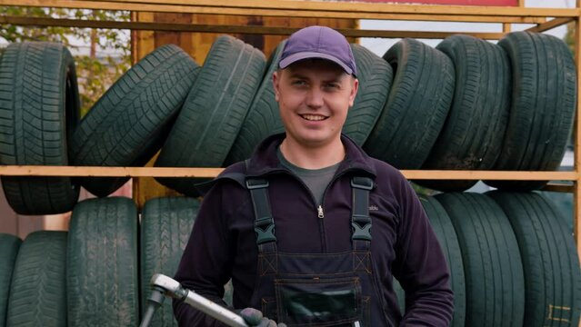Portrait of a smiling man Car mechanic with a balloon wrench in his hand dressed in work uniform on the background of car tires detailing car repair
