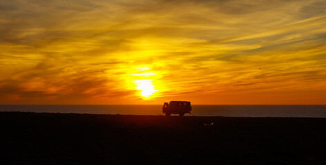 Silhouette of traveler camper on ocean coast at sunset