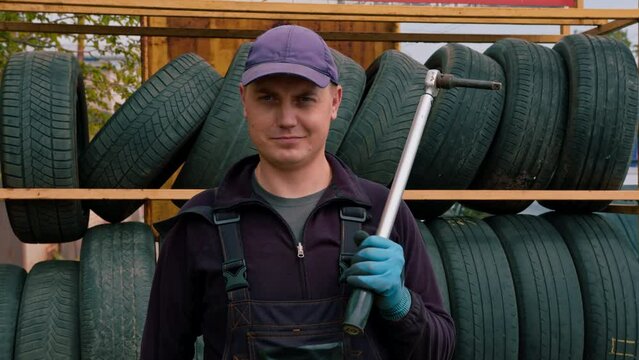 Portrait of a serious man Car mechanic with a balloon wrench in his hand dressed in work uniform on the background of car tires detailing car repair