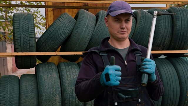 Portrait of a serious man Auto mechanic showing Thumb signal with a cylinder wrench in his hand on the background of car tires detailing auto repair