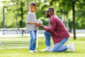 Portrait of happy father and son with ball while playing football on green grass in park.