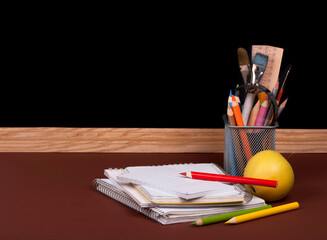 Magnifying glass, scissors, colored paper, textbooks, Apple, cubes, board, pencils, opened empty notebook against a dark background