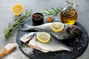Fresh sea bream fish with lemon, rosemary, olive oil and spices on a slate board, close up