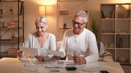 Family finance. Couple saving. Happy satisfied married man woman arranging money counting budget sitting table in light shadow room interior.