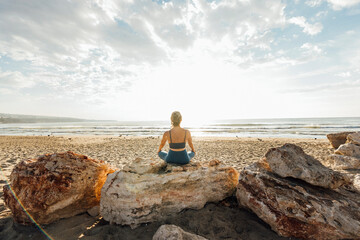 Woman meditating sitting on rock at beach