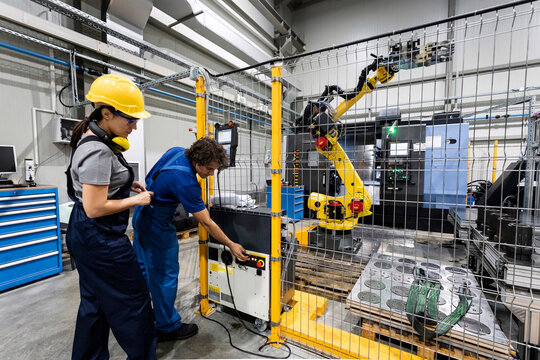 Maintenance engineers operating robotic arm in modern factory - Powered by Adobe