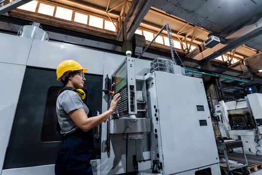 Maintenance engineer wearing hardhat using CNC Machine keypad in modern factory