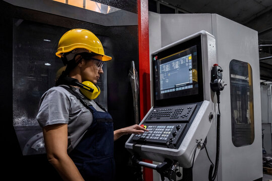 Engineer wearing hardhat operating CNC machine keypad in modern factory