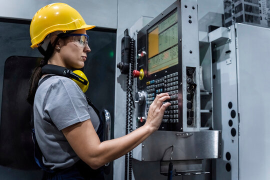 Maintenance engineer wearing hardhat operating machine keypad in modern factory