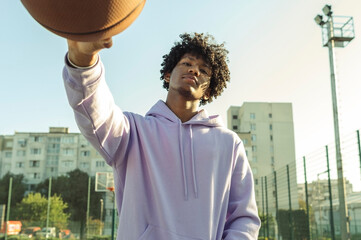 Confident athlete wearing purple hoodie holding basketball at sports court