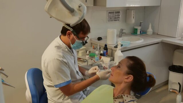 The young adult woman at the dentist appointment. The patient is in the dental chair with her mouth open while the dentist treats her teeth. Dentist's office. Health care