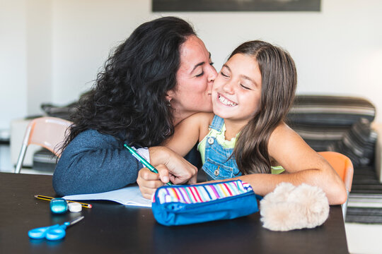 Mother kissing daughter doing homework