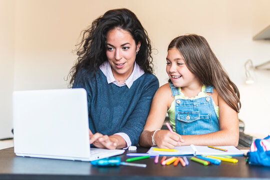 Freelancer mother showing daughter over laptop at table