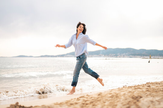 Happy Mature Woman Running Near Sea At Beach