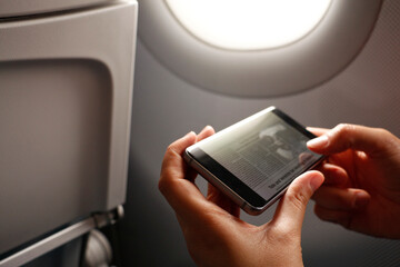 Hands of woman holding smart phone with news article on display in airplane