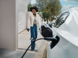 Smiling young woman standing by electric car at charging station