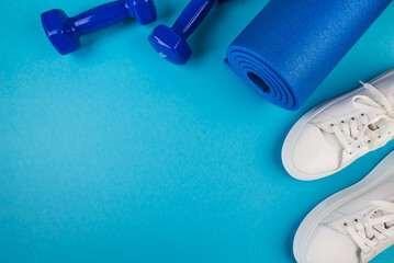 The concept of sports accessories. Photo of blue dumbbells and a blue exercise mat, white sneakers and other sports equipment.
