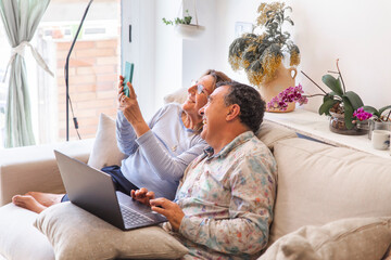 Happy senior couple spending leisure time with wireless technologies at home