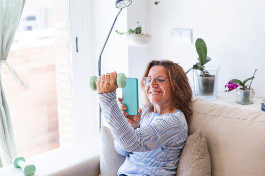 Woman taking picture of hand holding dumbbell through smart phone at home