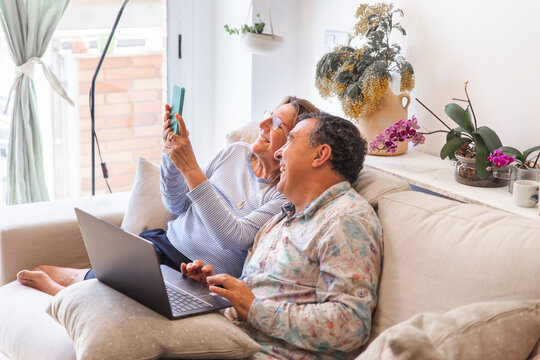 Happy senior couple spending leisure time with wireless technologies at home