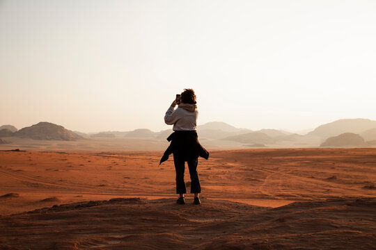 Young woman with smart phone photographing sunset in desert