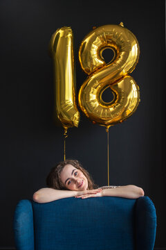Young woman leaning on chair with number 18 balloon on black backdrop