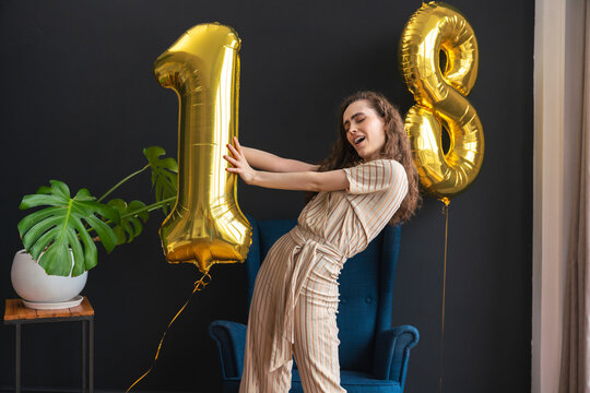 Playful young woman holding number 1 helium balloon at home