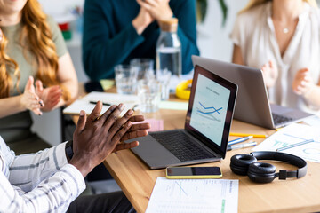 Businessman clapping hands in front of data on laptop at workplace
