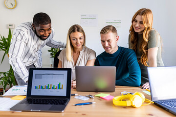 Smiling businessmen and businesswomen sharing laptop at office
