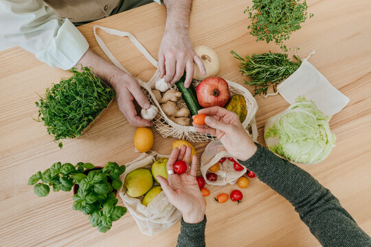 Couple unpacking fruits and vegetables from mesh bag - Powered by Adobe
