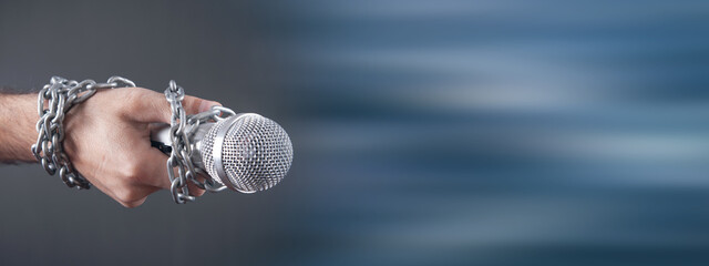 Human hand holding microphone tied with chains.