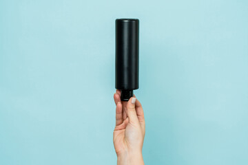 Woman's hand holding black bottle of cosmetic product for shower on blue background