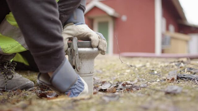 Sanitation worker wearing gloves opens up septic tank coupling outside house