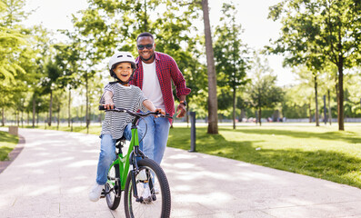 Happy ethnic family father teaches child  son  to ride bike in park  . - 609850162