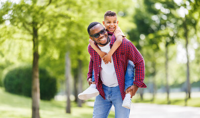 Happy ethnic family father and son have fun on walk in summer park.