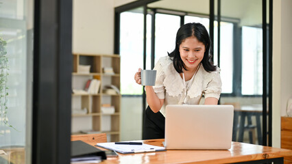 Attractive Asian businesswoman sipping coffee while working on her business tasks on the laptop