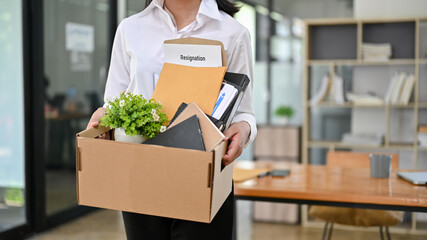 A female office worker with a cardboard box with her stuff and her resignation letter. - obrazy, fototapety, plakaty