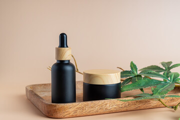 Cannabis face cream and serum or oil dropper concept. Natural cosmetic. CBD oil, THC tincture and hemp leaves on a wooden tray on beige background